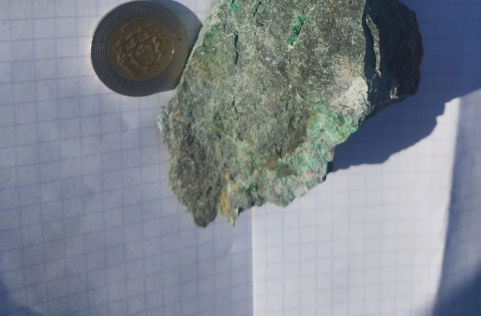 Échantillon de roche vert et gris posé à côté d’une pièce pour l’échelle