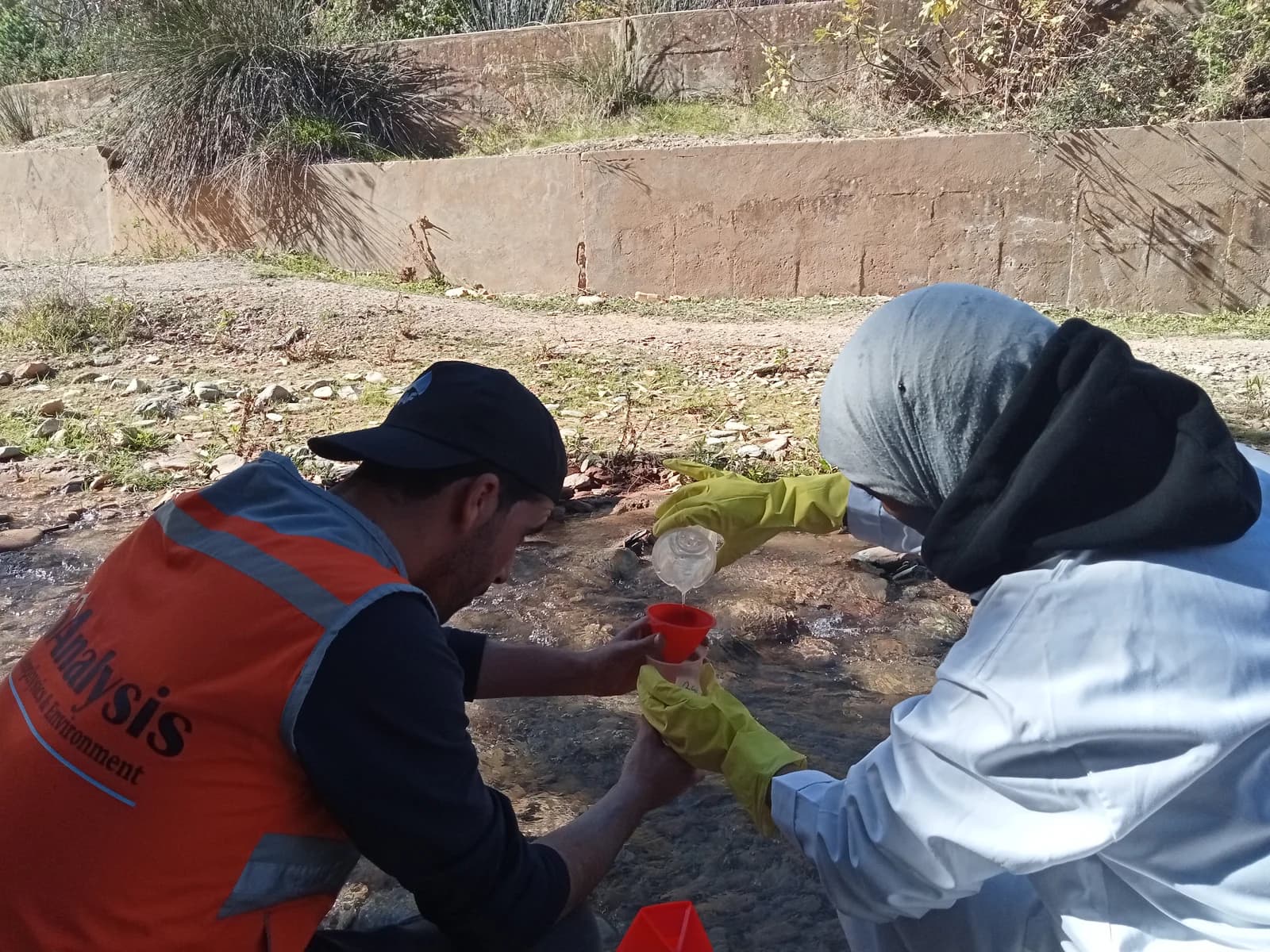 Deux membres de l’équipe prélèvent un échantillon d’eau sur le terrain.